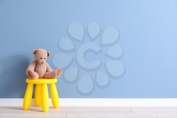 Stool with toy bear near color wall in children's room�