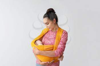 Young mother with little baby in sling on light background�