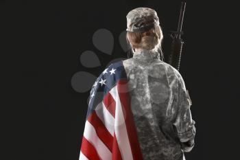 Young female soldier with USA flag on dark background, back view�