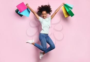 Portrait of jumping African-American woman with shopping bags on color background�