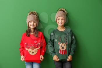 Little children in Christmas sweaters and knitted hats on color background�