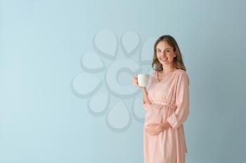 Beautiful pregnant woman with cup of tea on color background�