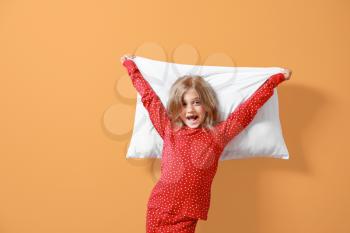 Happy little girl in pajamas and with pillow on color background�