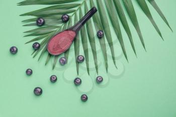 Spoon with powder and fresh acai berries on color background�