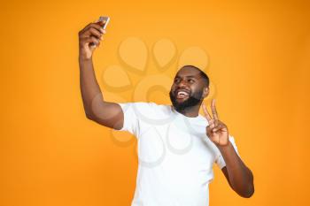 Happy African-American man taking selfie on color background�
