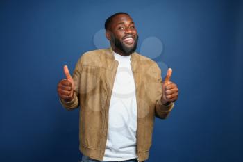 Happy African-American man showing thumb-up gesture on color background�