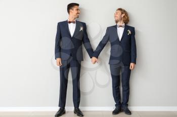 Portrait of happy gay couple on their wedding day against light wall�