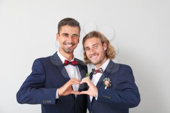 Happy gay couple making heart with their hands on wedding day against light background�