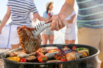 Man cooking tasty meat on barbecue grill outdoors, closeup�