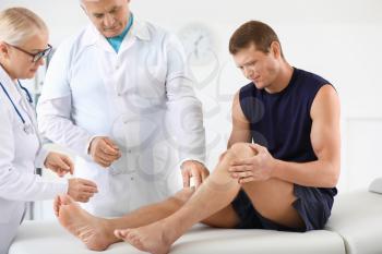 Mature doctors examining sportsman with joint pain in clinic�