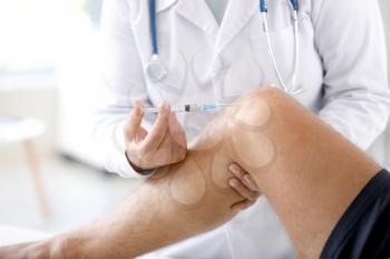 Doctor giving sportsman with joint pain injection in clinic, closeup�