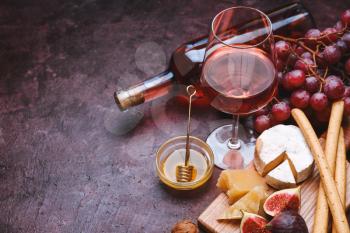 Glass and bottle of tasty wine with snacks on color background�