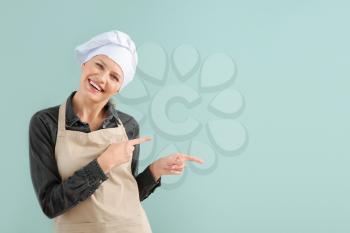 Beautiful female chef pointing at something on color background�