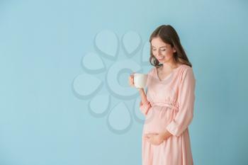 Beautiful pregnant woman with cup of tea on color background�