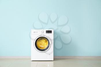 Modern washing machine with laundry near color wall�