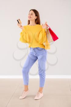 Beautiful young woman with shopping bags and credit card near light wall�