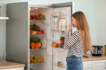 Woman feeling bad smell from fridge in kitchen�
