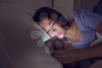 Teenage girl with mobile phone lying in bed at night�