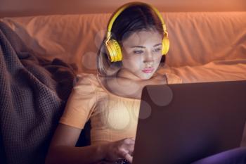 Teenage girl with laptop listening to music late in evening�