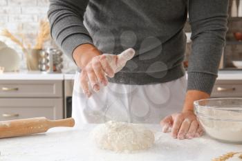 Man sprinkling dough with flour in kitchen�