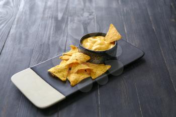 Board with tasty nachos and sauce on dark table�