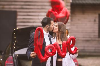 Happy young couple with air balloon in shape of word LOVE near car outdoors. Valentine's Day celebration�