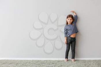 Little girl measuring height near grey wall�
