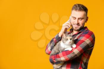 Man with cute cat talking by phone on color background�