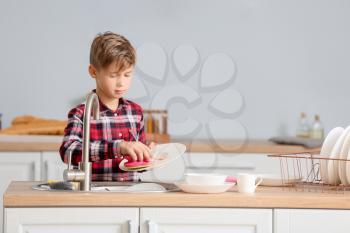 Little boy washing dishes in kitchen�