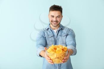 Handsome young man with tasty potato chips on color background�