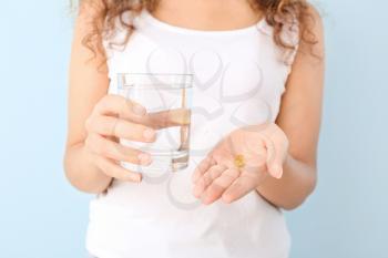 Young woman with fish oil and glass of water on color background, closeup�