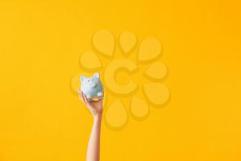 Female hand with piggy bank on color background�