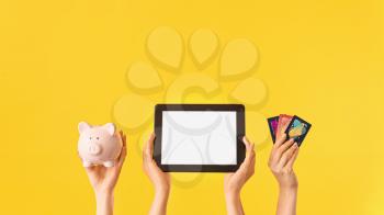 Female hands with piggy bank, credit cards and tablet computer on color background. Concept of online banking�