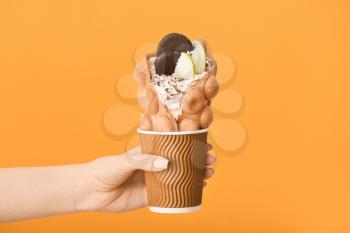 Female hand with delicious sweet bubble waffle on color background�