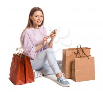 Young woman with mobile phone and shopping bags on white background�
