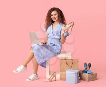 Young woman with laptop and new shoes on color background. Online shopping concept�