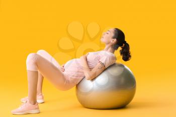 Young pregnant woman doing exercises with fitball on color background�