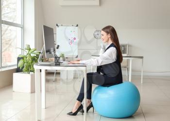 Businesswoman sitting on fitness ball while working in office�