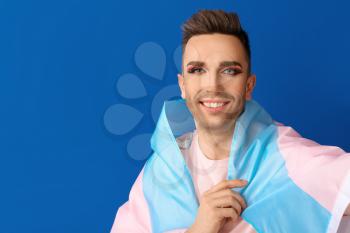 Portrait of young transgender woman with flag on color background�