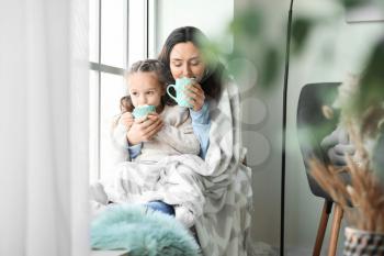 Woman and her little daughter with tasty cocoa drink near window at home�