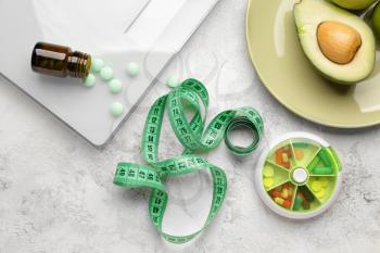 Weight loss pills, scales, fruits and measuring tape on light background�