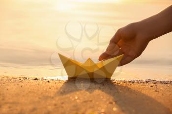 Woman putting origami boat on water surface near bank�