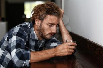 Depressed young man drinking alcohol in bar�