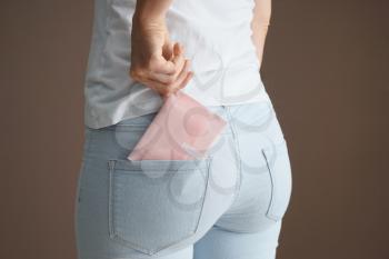 Woman putting menstrual pad into pocket on color background�