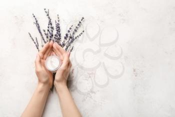 Hands of young woman with cream and lavender on light background�