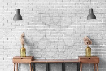 Wooden stand with decor and lamps near grey brick wall in room�