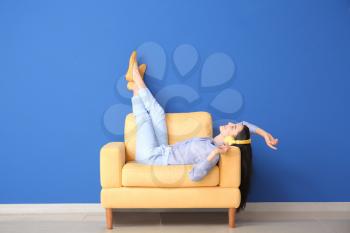 Young woman relaxing in armchair near color wall�