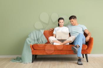 Young couple with laptop relaxing on sofa near color wall�