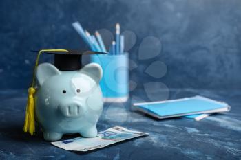 Piggy bank with graduation hat and money on table. Tuition fees concept�