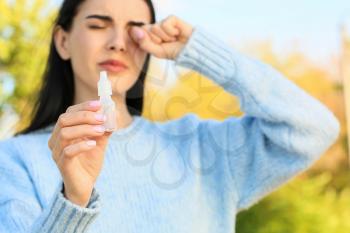 Young allergic woman with eye drops outdoors�
